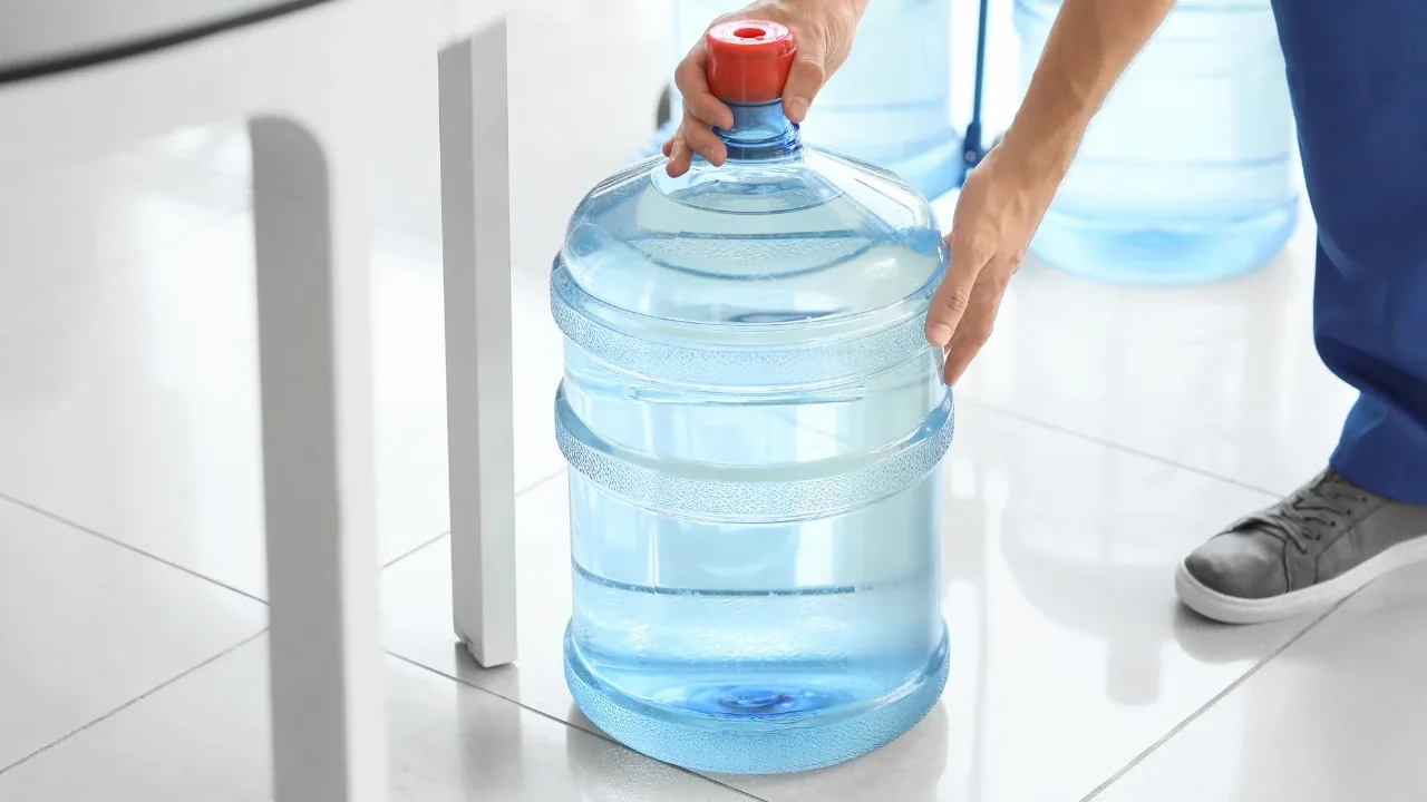 Persona colocando un bidón de agua de 20 litros en el piso